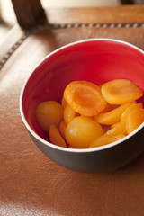 Peach halves in syrup, in a deep bowl,on a leather surface.