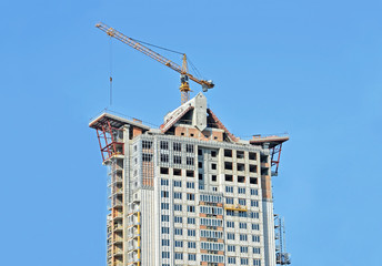 Fototapeta premium Building crane and building under construction against blue sky