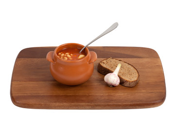 Soup in clay pot with bread and garlic on wooden kitchen board.