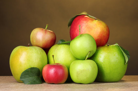 Many fresh organic apples on wooden table on yellow background