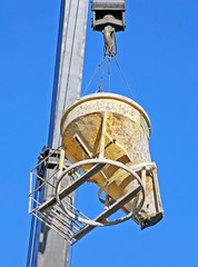 Mobile crane lifting concrete mixer container against blue sky
