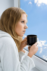 young beautiful girl drinking coffee by the window