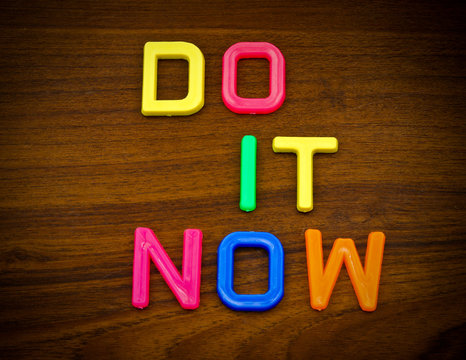 Do it now in colorful toy letters on wood background