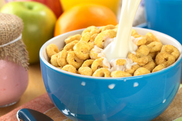 Pouring milk over a bowl full of honey flavored cereal loops