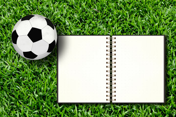 Football and blank notebook on Green Grass