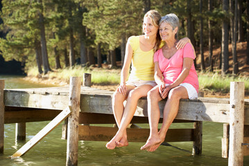 Mother and adult daughter sitting by lake