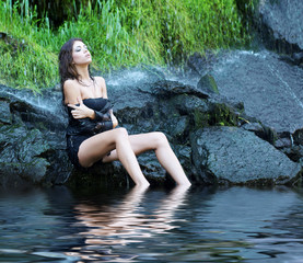Young and beautiful girl in bikini taking bath in a waterfall