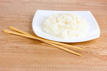 White bowl of cooked rice and chopsticks on wooden table