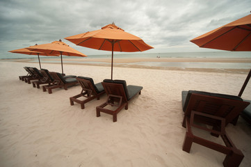 Orange umbrellas and chairs on sand beach.