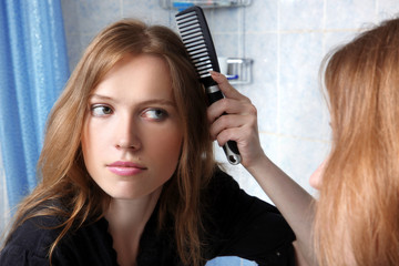Fototapeta premium young woman in bath at front of a mirror correcting hairs