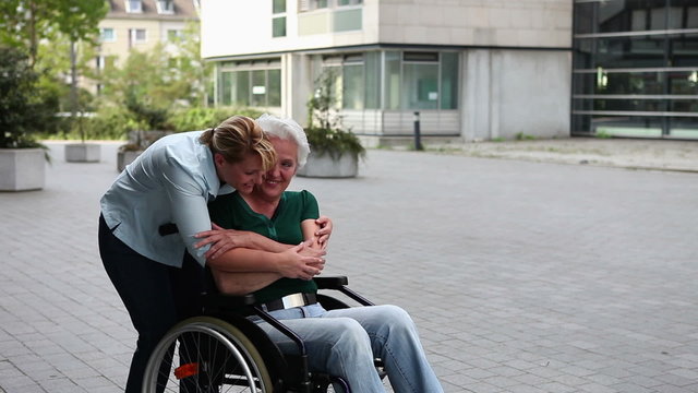 Nurse hugging woman in wheelchair