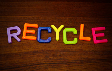 Recycle in colorful toy letters on wood background