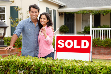 Hispanic couple outside home with sold sign - obrazy, fototapety, plakaty