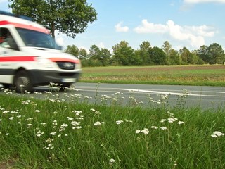 Krankenwagen fährt im Notfall schnell über Landstraße, Landschaft im Hintergrund, Niedersachsen,...