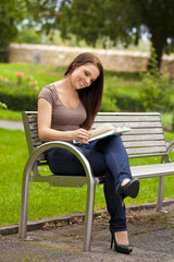 lächelnde hübsche junge Frau liest ein Buch im Park