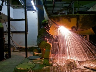 A workman flame cutting a lage metal tank