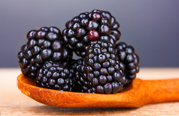 beautiful blackberries in wooden spoon on gray background