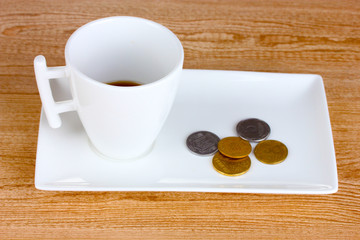 Empty cup of coffee with coins tip on wooden background