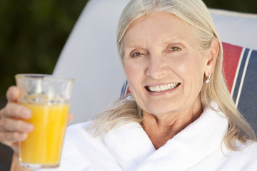 Happy Senior Woman in White Bathrobe Drinking Orange Juice