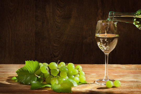 White Wine Pouring Down To The Glass With Grapes