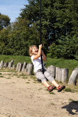 Fun in the park. Girl pulls down the hill on a rope - obrazy, fototapety, plakaty