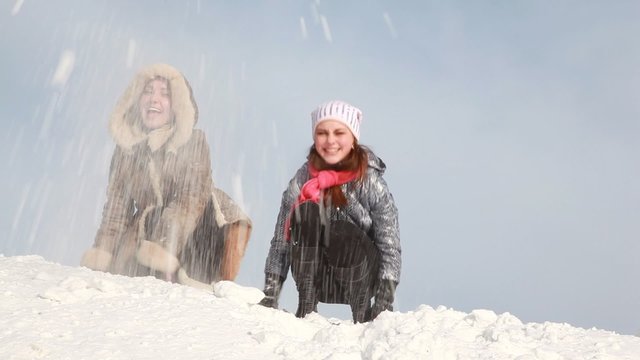 The women are sitting and throwing snow