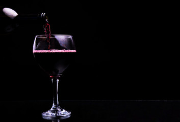 Red wine pouring into wine glass against black background