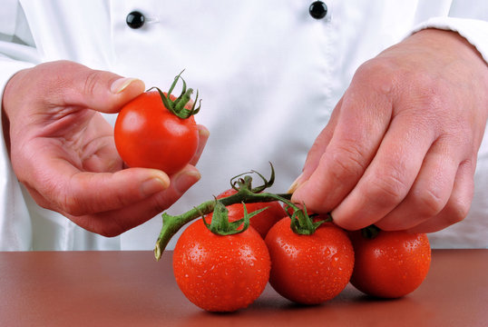K&ouml;chin h&auml;lt eine Tomate und Party Tomaten liegen auf einer bra