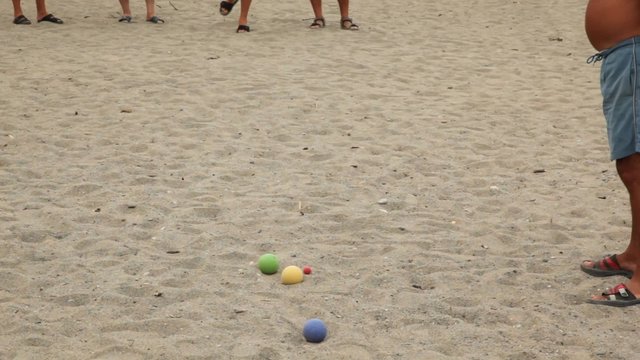 Five men in flip-flops throw balls by turns on beach