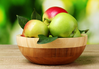 Fresh organic apples in plate on wooden table outside