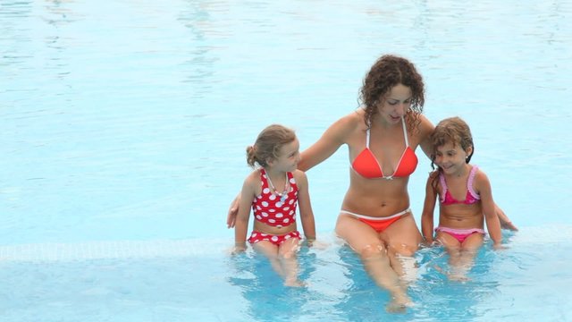 Woman with two daughters communicate in pool