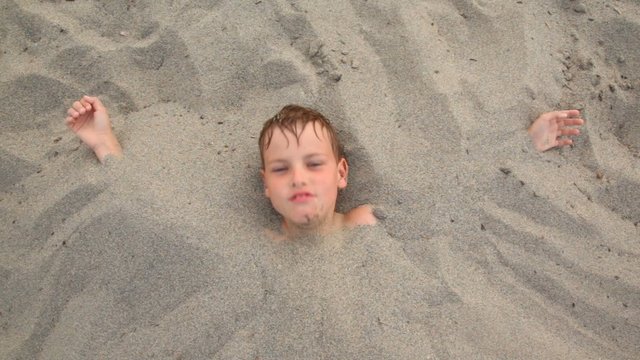 Top View Head Of Boy Lies Smiles Buried Up With Sand