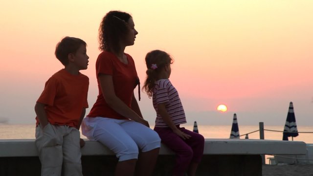 Mom and kids are sitting on bench and sun rises