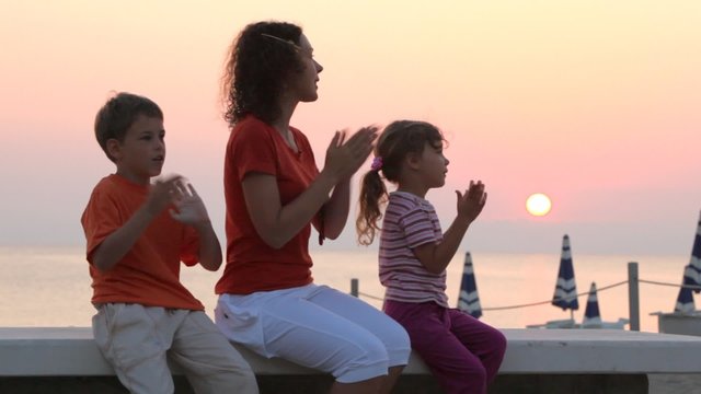 Mom and kids are sitting on bench and claping hands