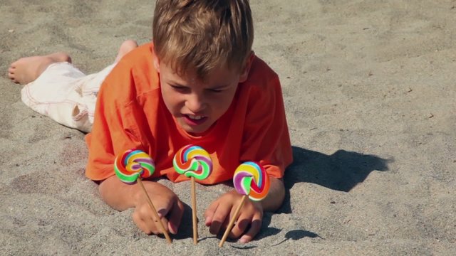 boy lying on the sand, in front of him three candy