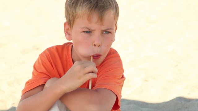 The boy sitting on the sand and eating candy