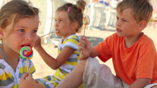 Three kids eating lolly candy sitting on sand