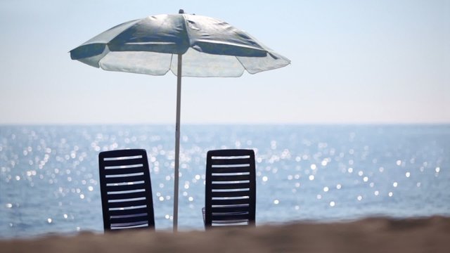 Two deckchairs stand on beach under parasol