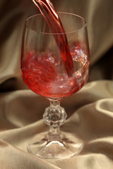 red wine pouring into crystal wine glass on gold background