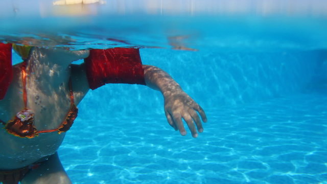 Little girl with inflatable arm ruffles swims in pool