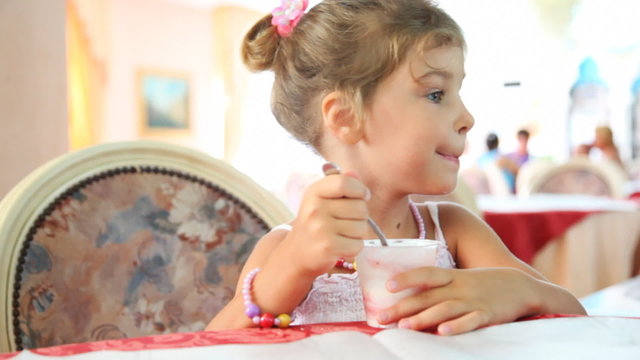 Little girl eats yogurt with spoon in cup at table