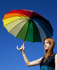 Redhead girl with umbrella at blue sky background.