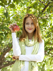 Beautiful young redhead woman standing near the apple tree.