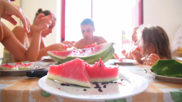 Sliced watermelon on plate and family around table eat it
