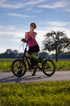 Frau steht mit Streetstepper und Sonnenbrille auf Fahrradweg