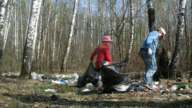 Two children collect trash to garbage bags in forest