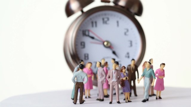 Little toy people stand in front of big clock