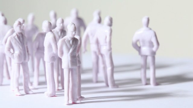 Group of little unpainted toy humans stand and drop shadows
