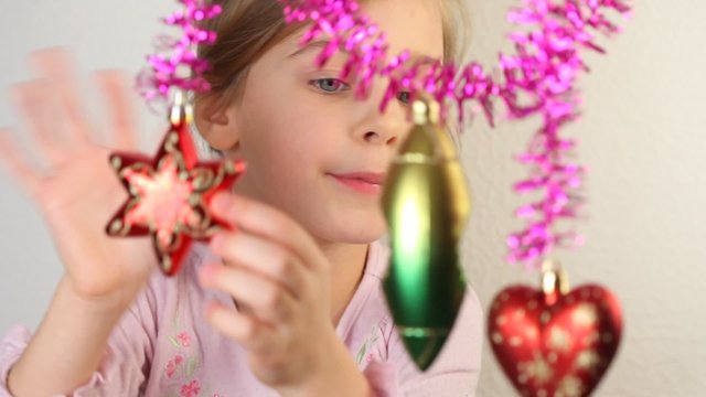 Little girl examine christmas-tree decoration, which hang.
