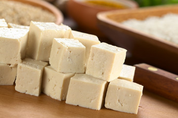 Raw tofu cut in dices on wooden board